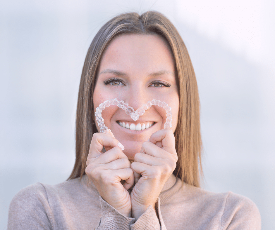 Happy adult woman displaying Invisalign clear aligners shaped like a heart
